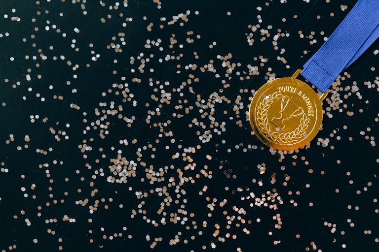 Close-up of a gold medal with blue ribbon and confetti on a black surface, symbolizing victory.