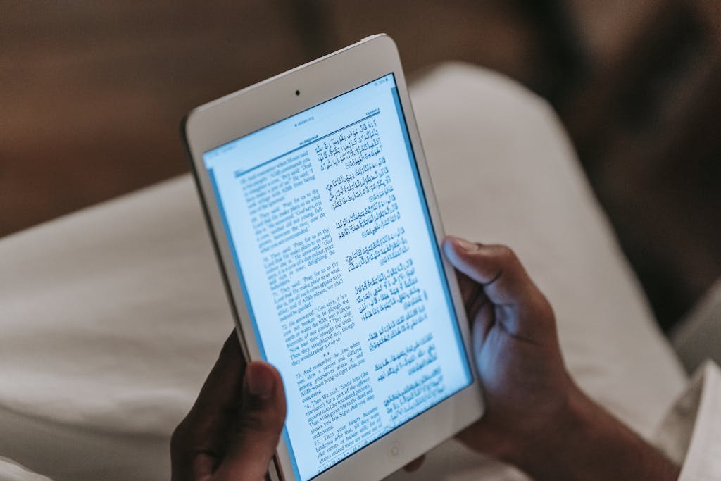 Crop unrecognizable person in casual clothes reading text on tablet against blurred background in room